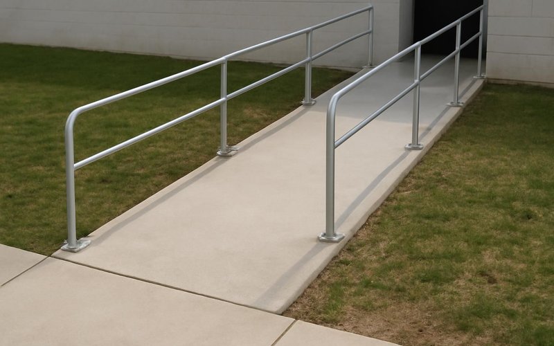 AI concept: A gently sloped concrete accessibility ramp with a completely flush smooth ground approach and secure handrails